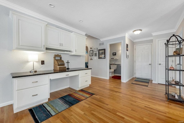 home office with crown molding, built in desk, a textured ceiling, and light wood-type flooring