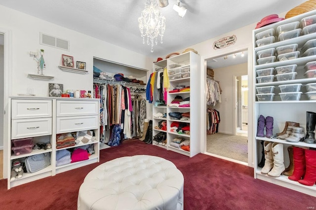 spacious closet featuring an inviting chandelier and dark colored carpet