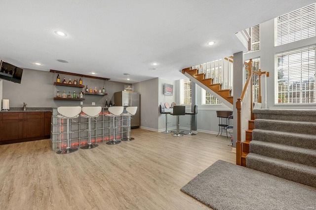 bar with stainless steel fridge with ice dispenser and light hardwood / wood-style flooring