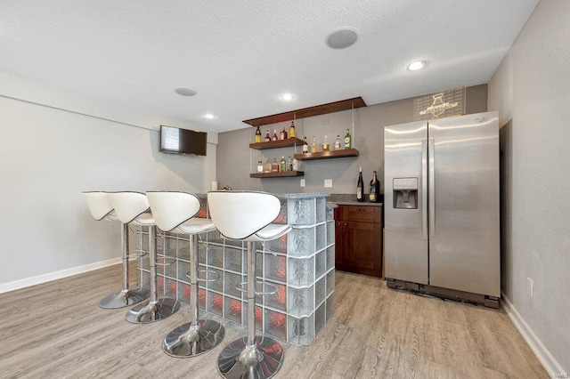 bar with stainless steel fridge with ice dispenser, a textured ceiling, and light wood-type flooring