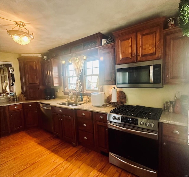 kitchen with appliances with stainless steel finishes, sink, and light wood-type flooring