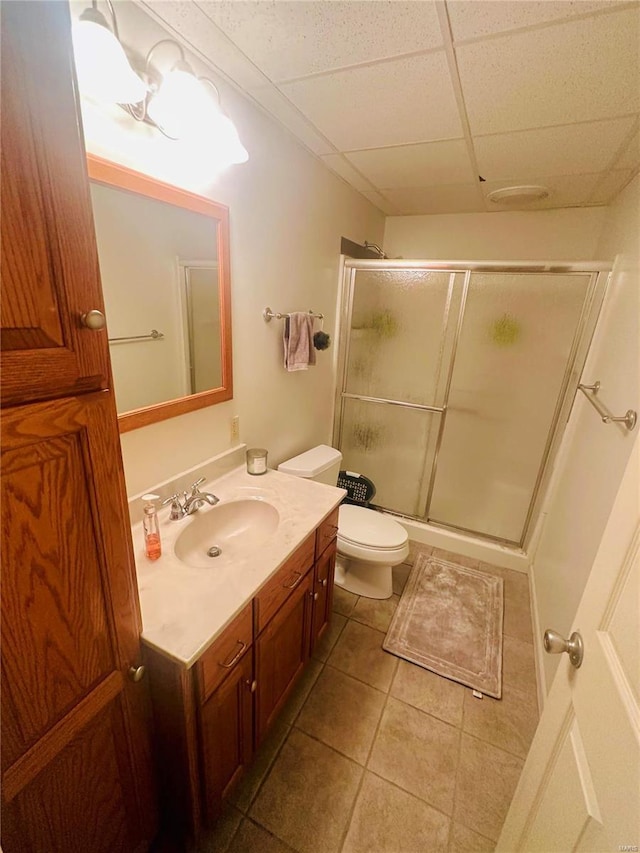 bathroom featuring a paneled ceiling, vanity, toilet, a shower with door, and tile patterned floors