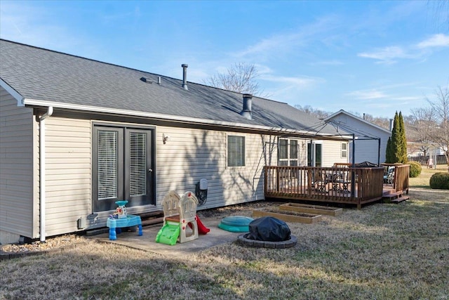 back of property featuring a wooden deck, a fire pit, and a lawn