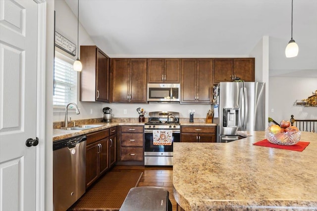 kitchen featuring dark wood-type flooring, sink, dark brown cabinets, hanging light fixtures, and appliances with stainless steel finishes