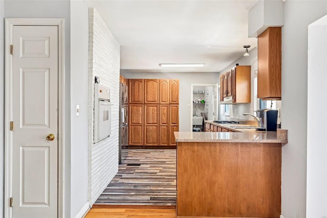 kitchen with sink, white oven, kitchen peninsula, and light wood-type flooring