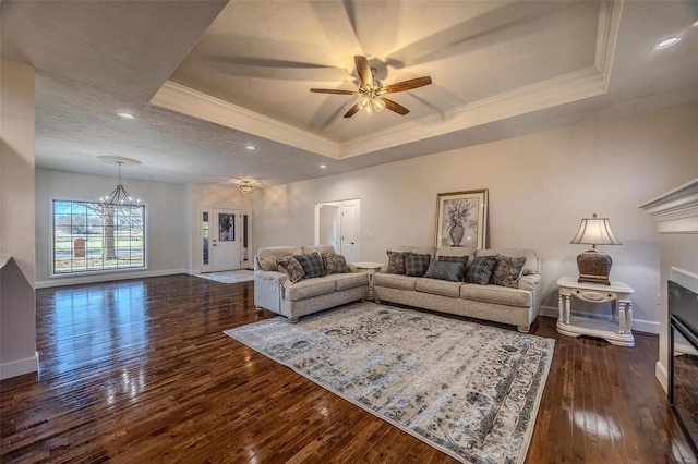 living room featuring dark hardwood / wood-style flooring, a tray ceiling, ceiling fan with notable chandelier, and crown molding