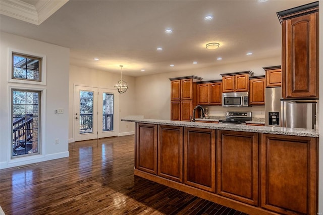 kitchen featuring pendant lighting, dark wood-type flooring, a kitchen island with sink, stainless steel appliances, and a notable chandelier