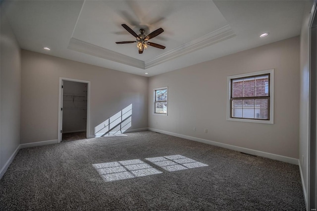 empty room with crown molding, ceiling fan, a tray ceiling, and dark carpet