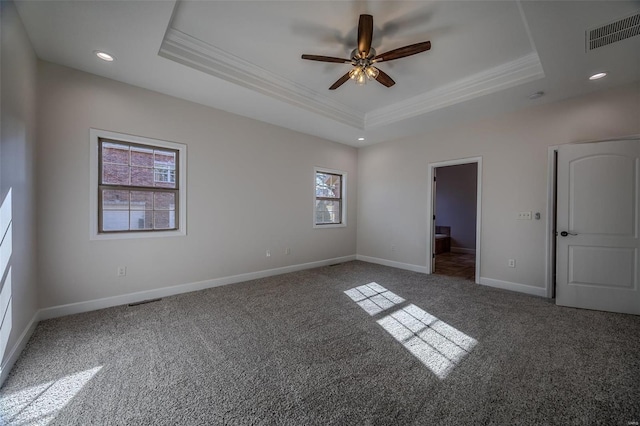 unfurnished bedroom with ceiling fan, ensuite bathroom, a tray ceiling, ornamental molding, and dark carpet