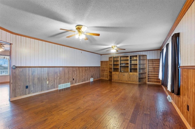 unfurnished living room featuring wooden walls, ornamental molding, ceiling fan, dark wood-type flooring, and a textured ceiling