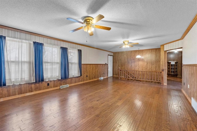 empty room with crown molding, wood-type flooring, a textured ceiling, and wooden walls