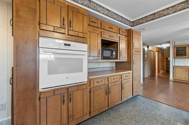 kitchen with black microwave, dark wood-type flooring, oven, and a textured ceiling