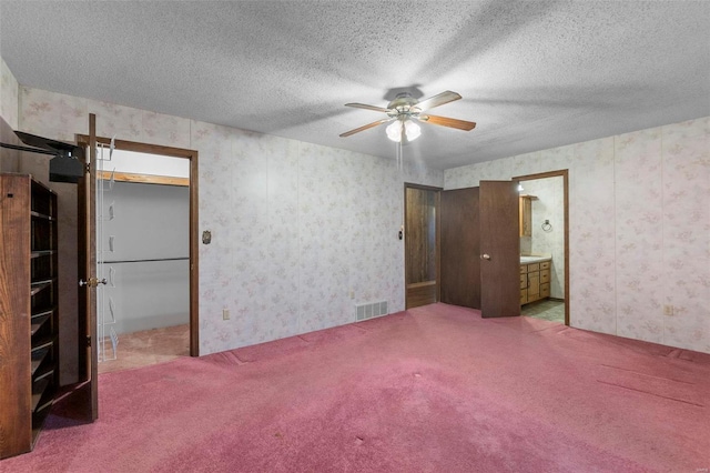 unfurnished bedroom featuring ensuite bath, carpet floors, a textured ceiling, and ceiling fan