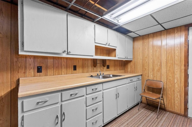 kitchen with sink, wooden walls, white cabinets, and a paneled ceiling