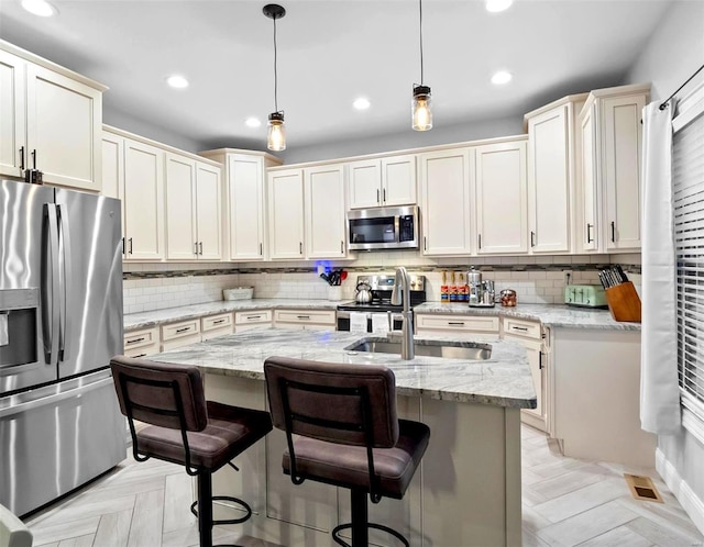 kitchen featuring an island with sink, appliances with stainless steel finishes, and light stone counters