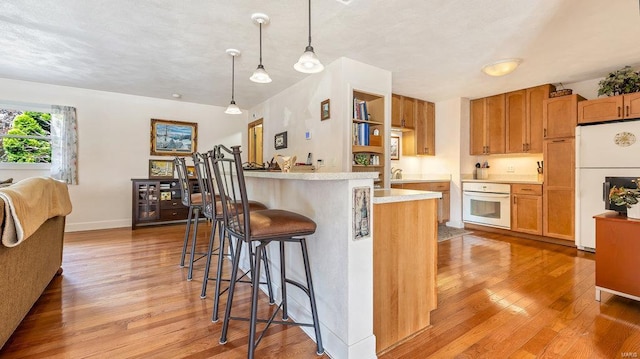 kitchen with a breakfast bar, pendant lighting, sink, light hardwood / wood-style floors, and white appliances