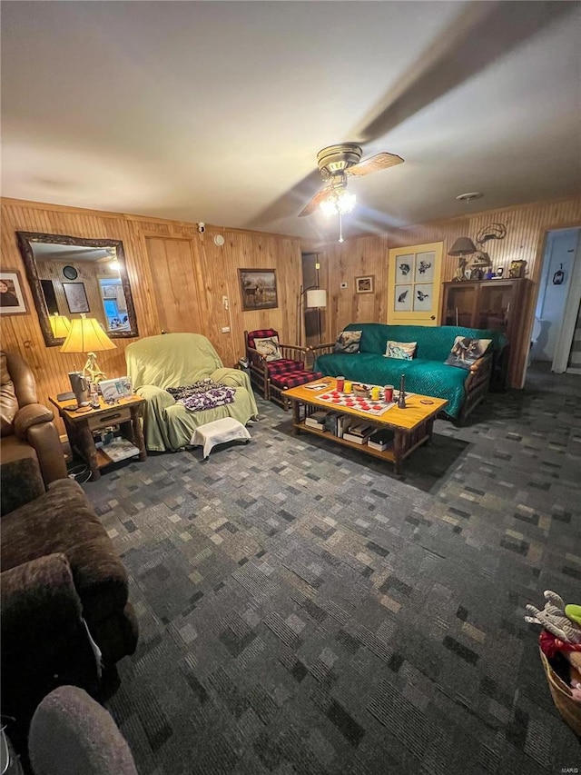 rec room featuring ceiling fan, wooden walls, and dark colored carpet