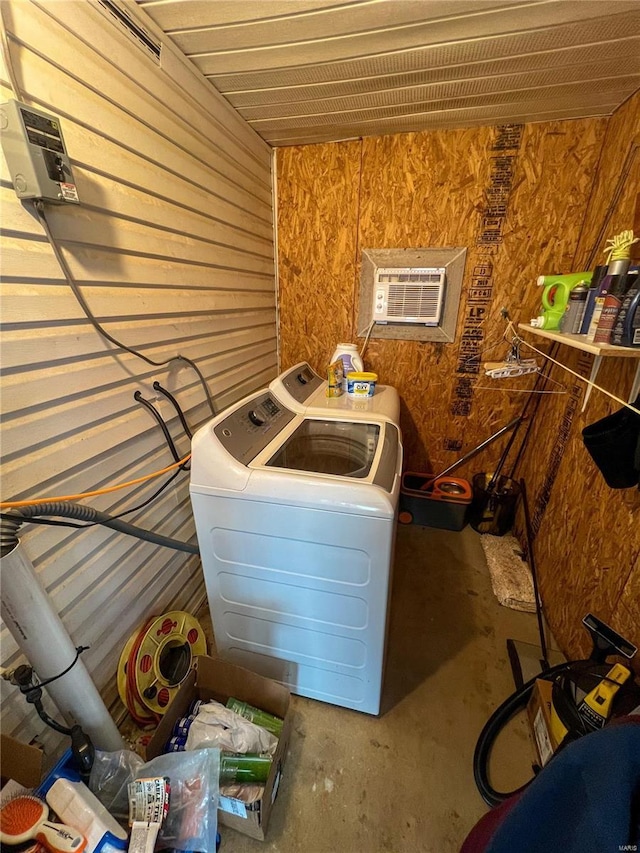 washroom with washer and dryer, a wall unit AC, and wood walls