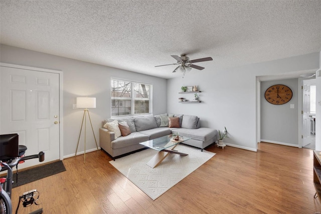 living room featuring ceiling fan, light hardwood / wood-style floors, and a textured ceiling