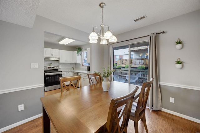 dining area featuring light hardwood / wood-style floors, a textured ceiling, and a notable chandelier