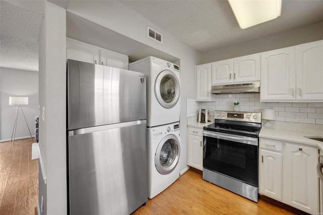 kitchen featuring white cabinetry, backsplash, stainless steel appliances, stacked washer and clothes dryer, and light hardwood / wood-style floors