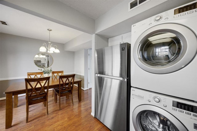 clothes washing area with a textured ceiling, light hardwood / wood-style floors, a chandelier, and stacked washing maching and dryer