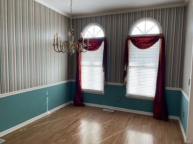 unfurnished dining area with crown molding, a chandelier, and hardwood / wood-style floors