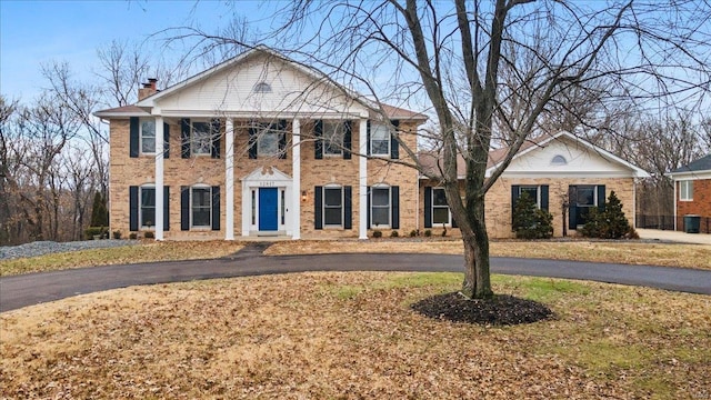 greek revival house featuring brick siding and a chimney