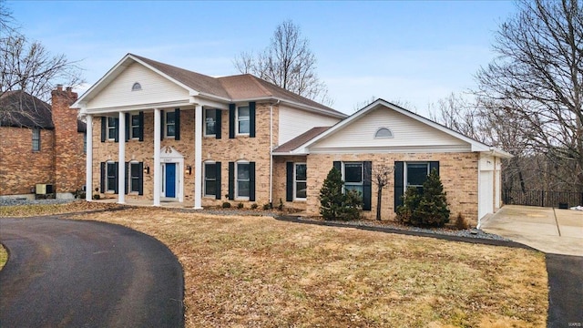 greek revival inspired property with brick siding, driveway, and a front yard