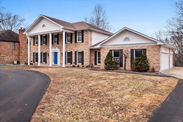 neoclassical home with a garage, brick siding, and driveway