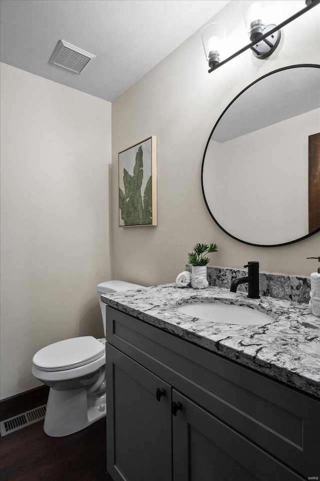 bathroom with vanity, toilet, wood finished floors, and visible vents