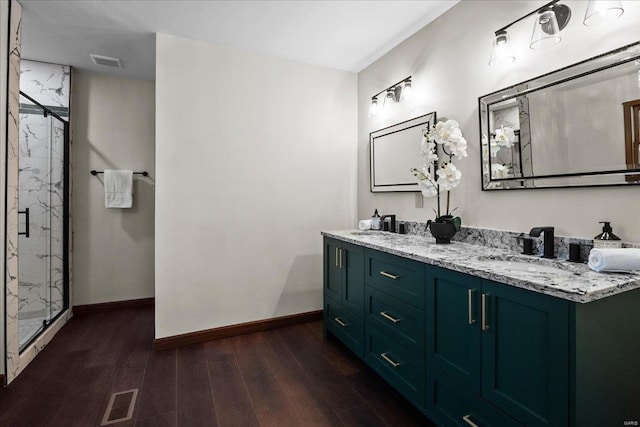 full bath featuring a marble finish shower, visible vents, a sink, and wood finished floors