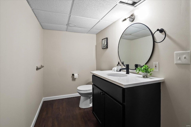 bathroom with toilet, a drop ceiling, wood finished floors, baseboards, and vanity