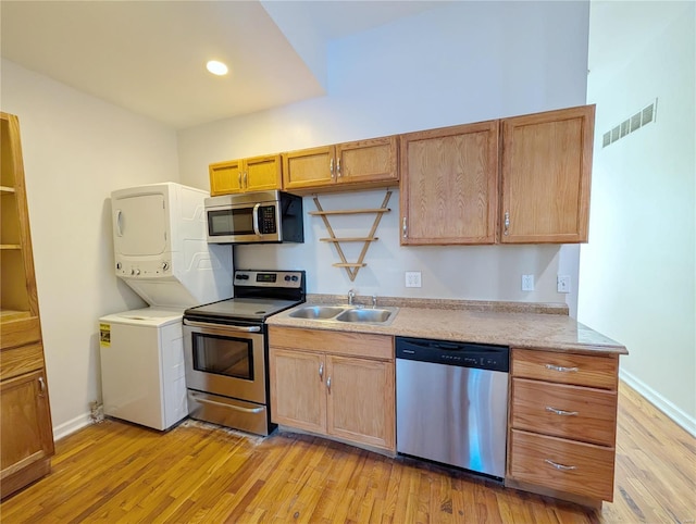 kitchen featuring stainless steel appliances, stacked washer / dryer, sink, and light hardwood / wood-style flooring