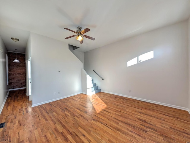 unfurnished living room with hardwood / wood-style flooring, brick wall, and ceiling fan