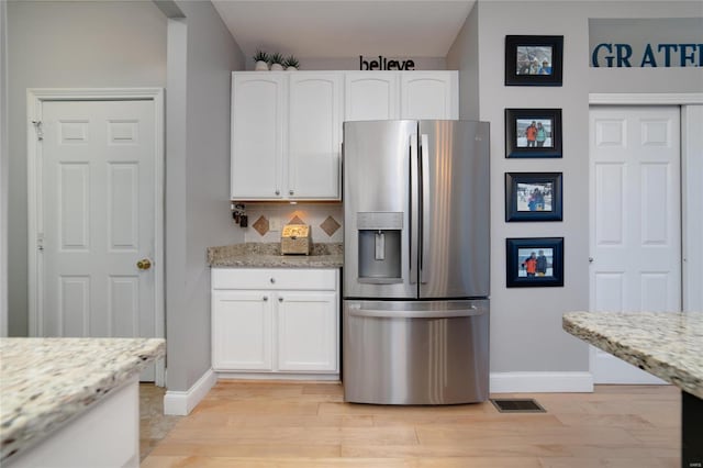 kitchen featuring white cabinetry, light stone countertops, stainless steel fridge, and light hardwood / wood-style floors