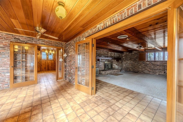 interior space featuring beam ceiling, wooden ceiling, brick wall, a fireplace, and ceiling fan with notable chandelier