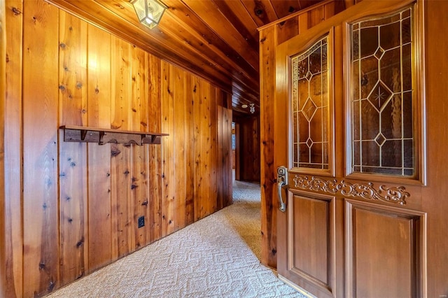 hall featuring carpet flooring, wooden ceiling, and wooden walls