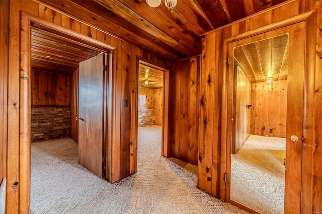 hall featuring wooden walls, light carpet, and wood ceiling