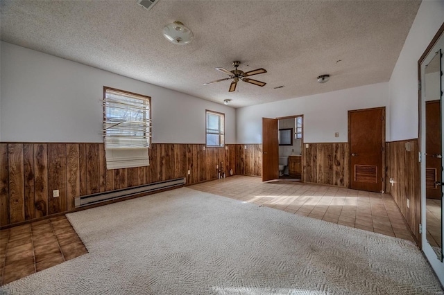 carpeted spare room with ceiling fan, a baseboard heating unit, wooden walls, and a textured ceiling