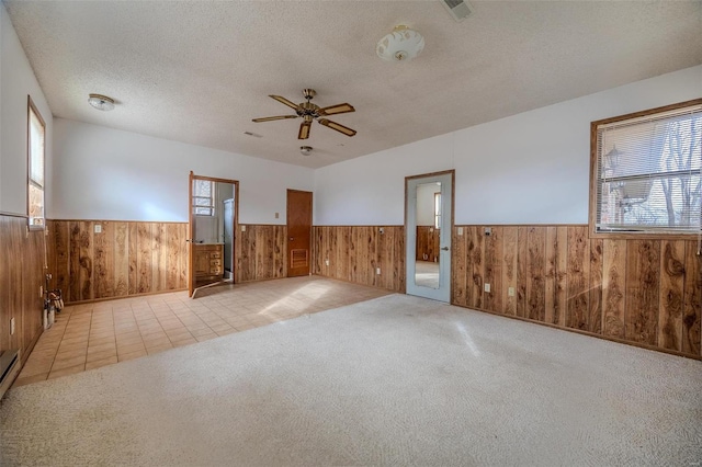 carpeted empty room with ceiling fan, a textured ceiling, and wood walls