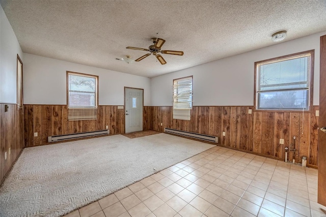 carpeted empty room featuring a baseboard heating unit, wooden walls, a textured ceiling, and ceiling fan