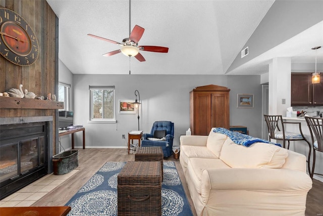 living room featuring vaulted ceiling, a textured ceiling, light wood-type flooring, ceiling fan, and a fireplace