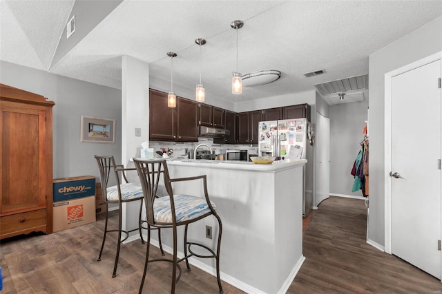 kitchen with dark hardwood / wood-style floors, pendant lighting, a breakfast bar area, white refrigerator with ice dispenser, and kitchen peninsula