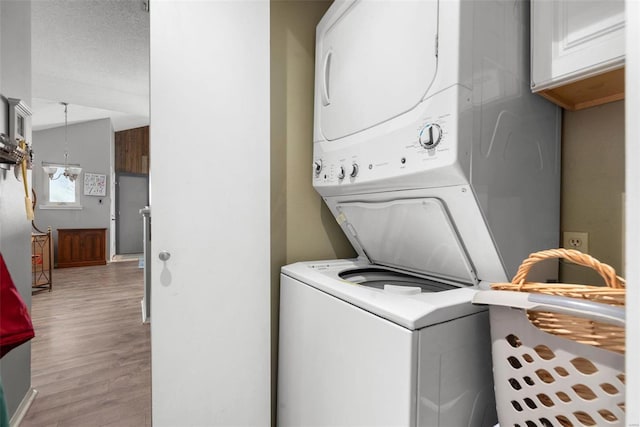 laundry area featuring stacked washer / dryer, a textured ceiling, and light hardwood / wood-style floors