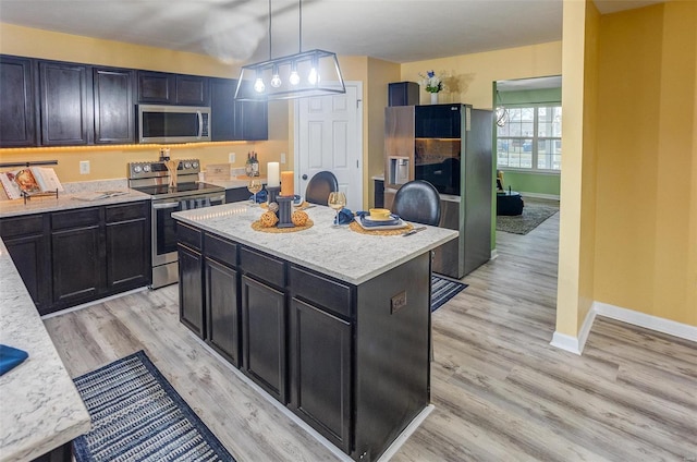 kitchen with appliances with stainless steel finishes, hanging light fixtures, a center island, light hardwood / wood-style floors, and light stone countertops