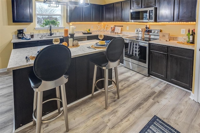 kitchen featuring a kitchen island, appliances with stainless steel finishes, sink, a breakfast bar area, and light stone countertops