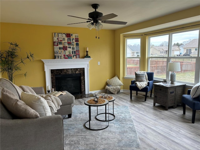 living room featuring a high end fireplace, ceiling fan, and light wood-type flooring