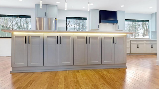 kitchen featuring decorative light fixtures, light wood-type flooring, stainless steel fridge, and a kitchen island