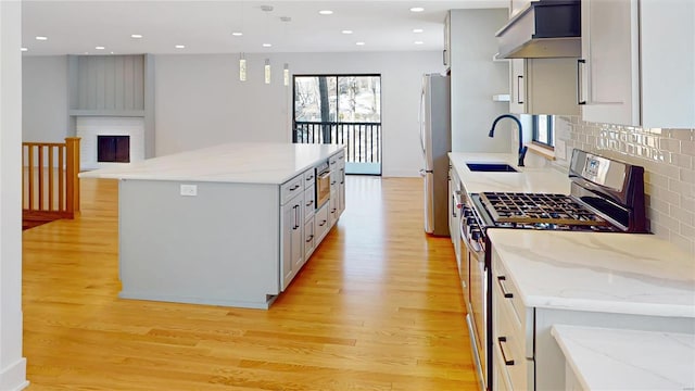 kitchen featuring appliances with stainless steel finishes, light stone counters, a fireplace, a kitchen island, and exhaust hood